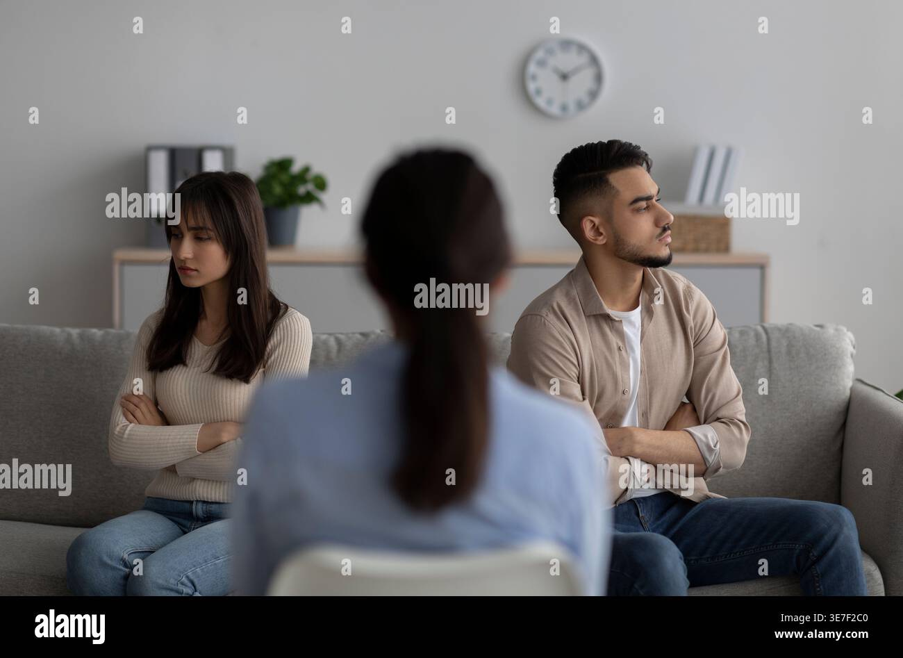 Couple du moyen-Orient regardant loin tout en s'asseyant dos à dos sur le canapé devant la thérapeute féminine en clinique Banque D'Images