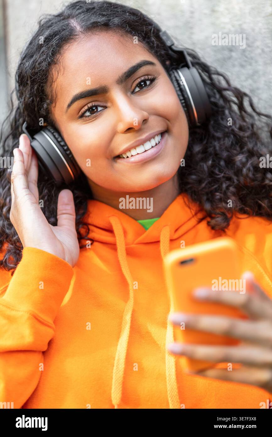 Femme noire souriante écoutant de la musique avec des écouteurs debout à l'extérieur Banque D'Images