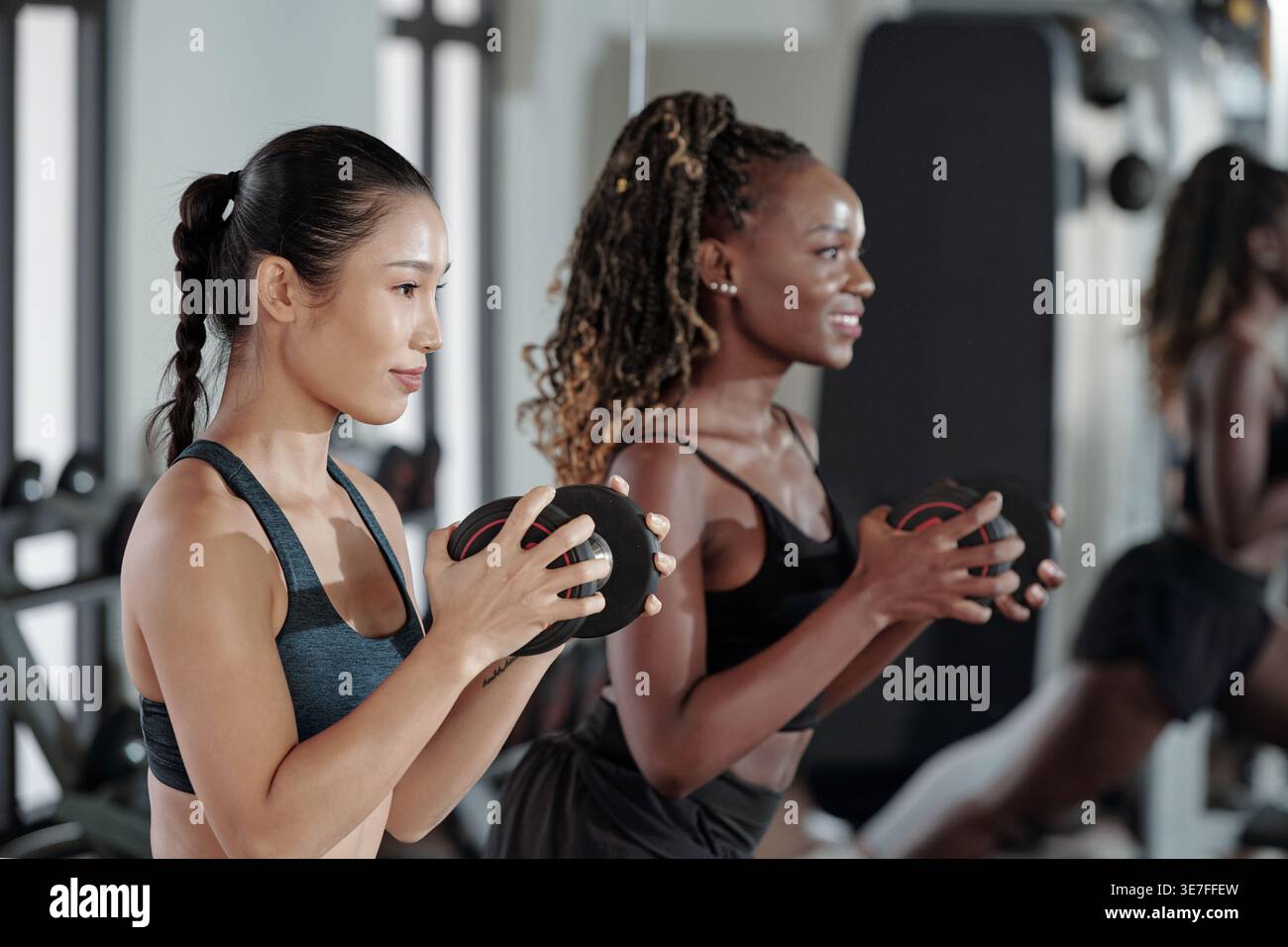 Amies asiatiques et noires faisant des fentes avec des haltères dans le gymnase Banque D'Images