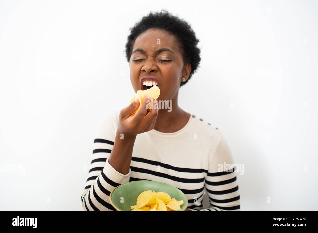 Femme noire mangeant des frites sur un bol avec les yeux fermés debout sur fond blanc Banque D'Images