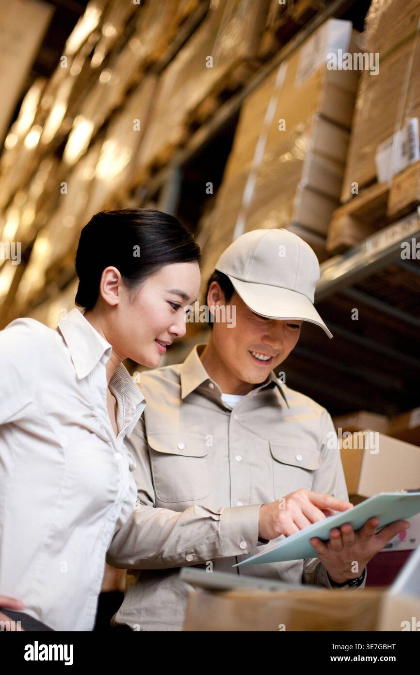 Travailleur chinois masculin et féminin tenant une planche à pince vérifiant les stocks debout dans l'entrepôt Banque D'Images