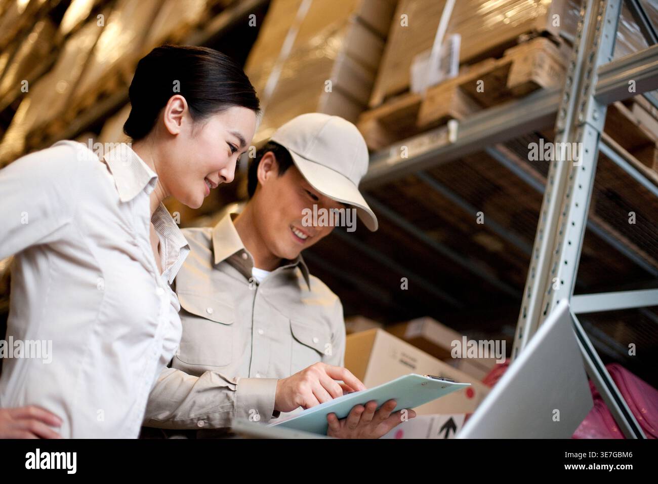 Travailleur chinois masculin et féminin tenant une planche à pince vérifiant les stocks debout dans l'entrepôt Banque D'Images