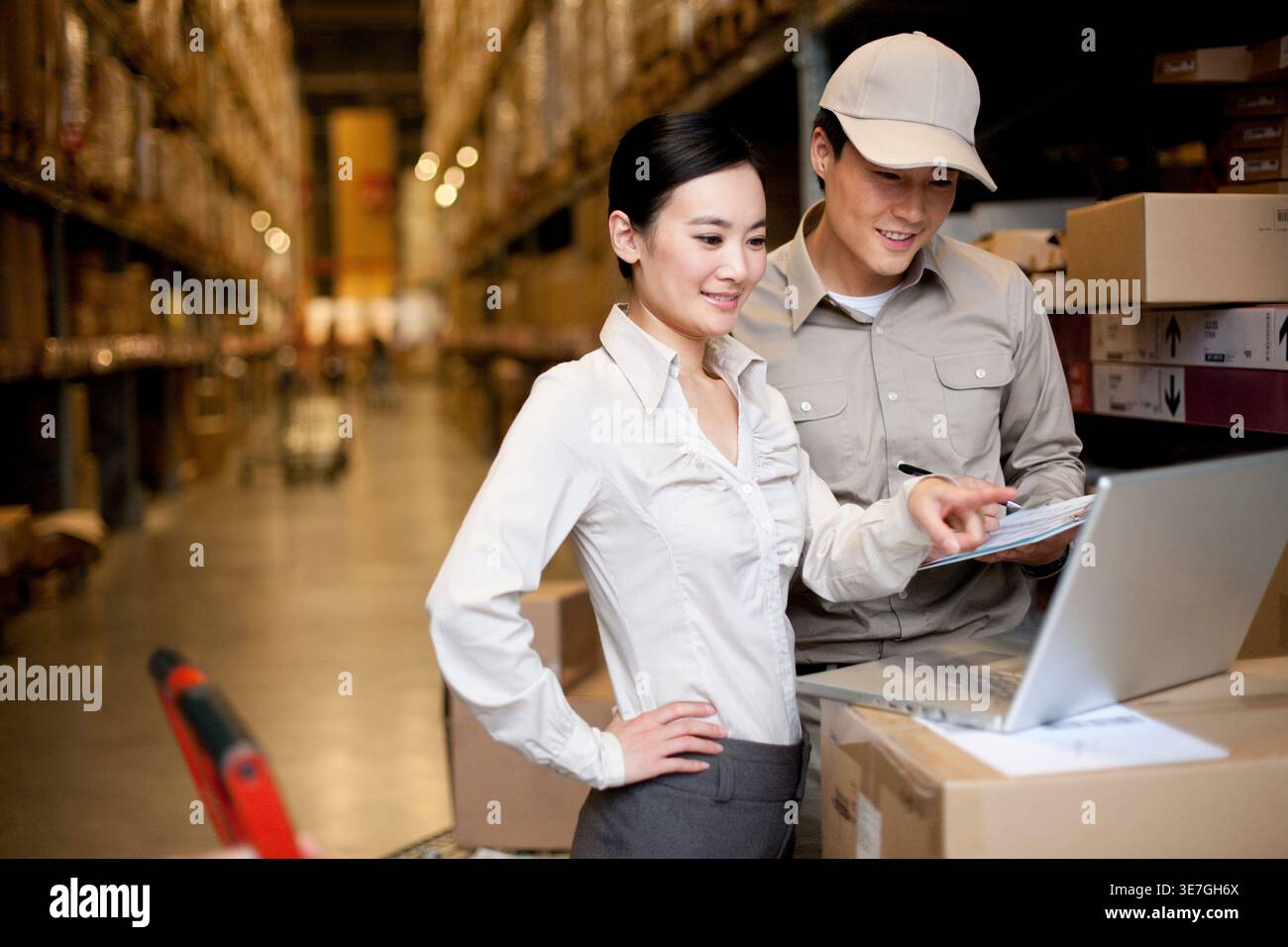 Travailleur chinois souriant masculin et féminin vérifiant les stocks sur ordinateur portable debout dans l'entrepôt Banque D'Images