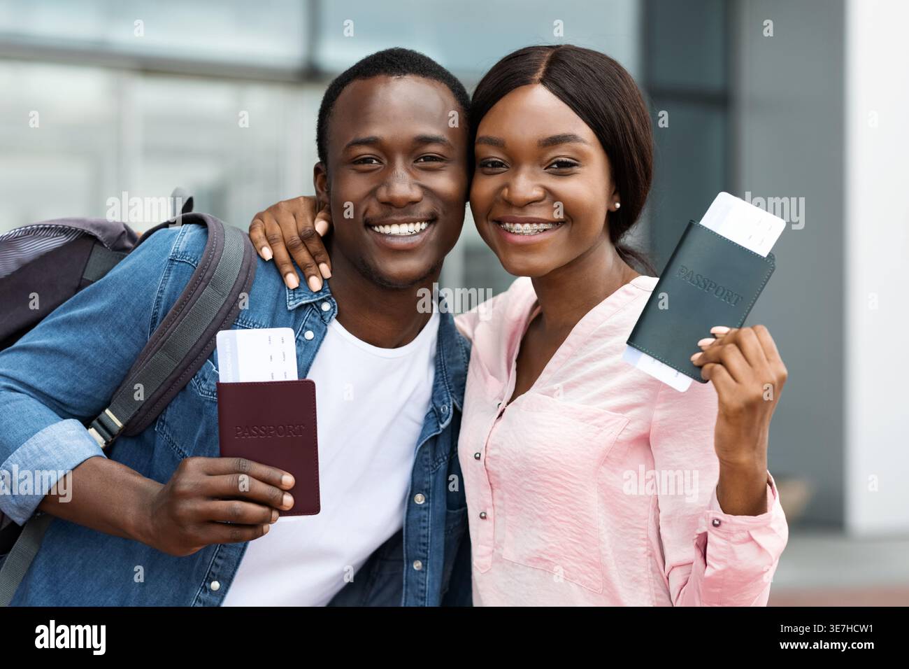 Couple noir souriant tenant des passeports avec billet d'avion debout près l'un de l'autre à l'extérieur de l'aéroport Banque D'Images
