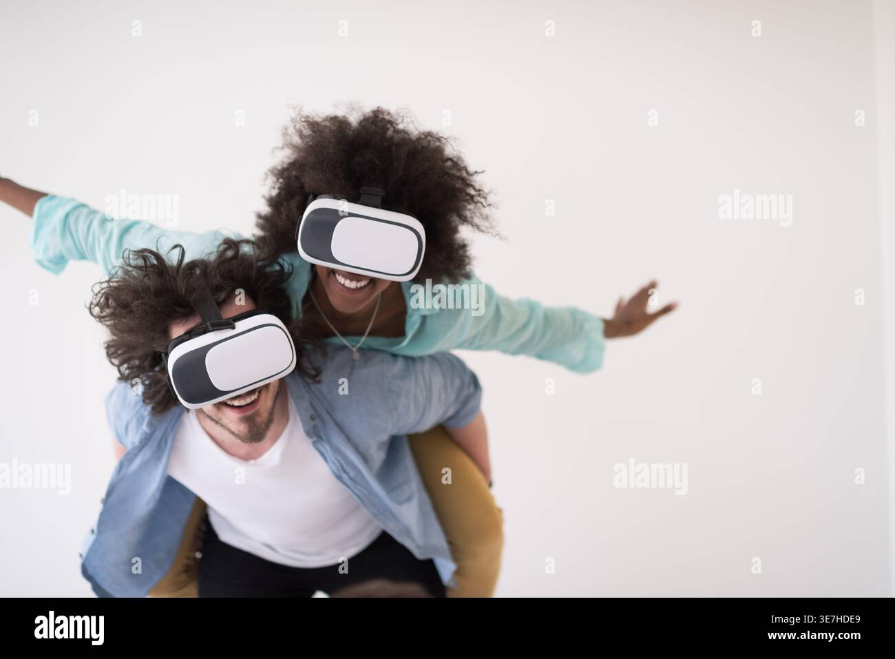 Couple noir et caucasien portant des casques VR ayant un plaisir piggyback équitation et expérimentant la réalité virtuelle sur fond blanc en studio Banque D'Images