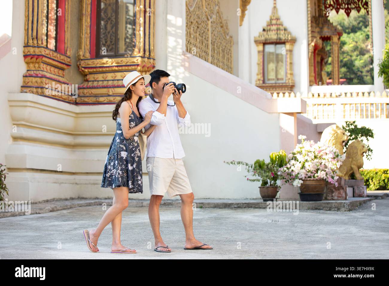 Joyeux couple chinois prenant des photos à l'aide de l'appareil photo DLSR tout en se tenant près du temple à l'extérieur Banque D'Images