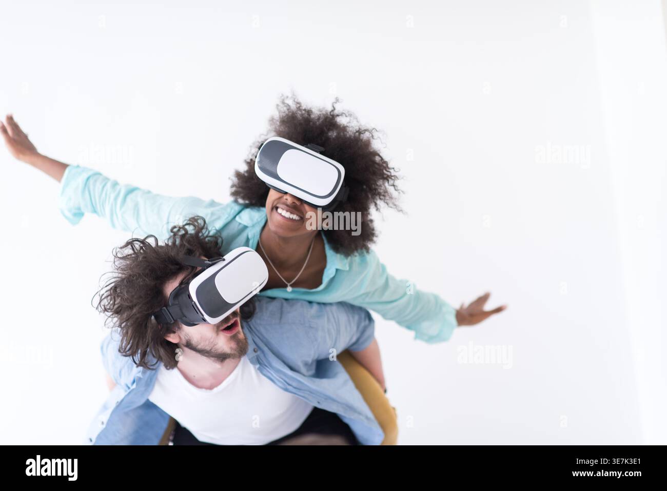 Couple noir et caucasien portant des casques VR ayant un plaisir piggyback équitation et expérimentant la réalité virtuelle sur fond blanc en studio Banque D'Images