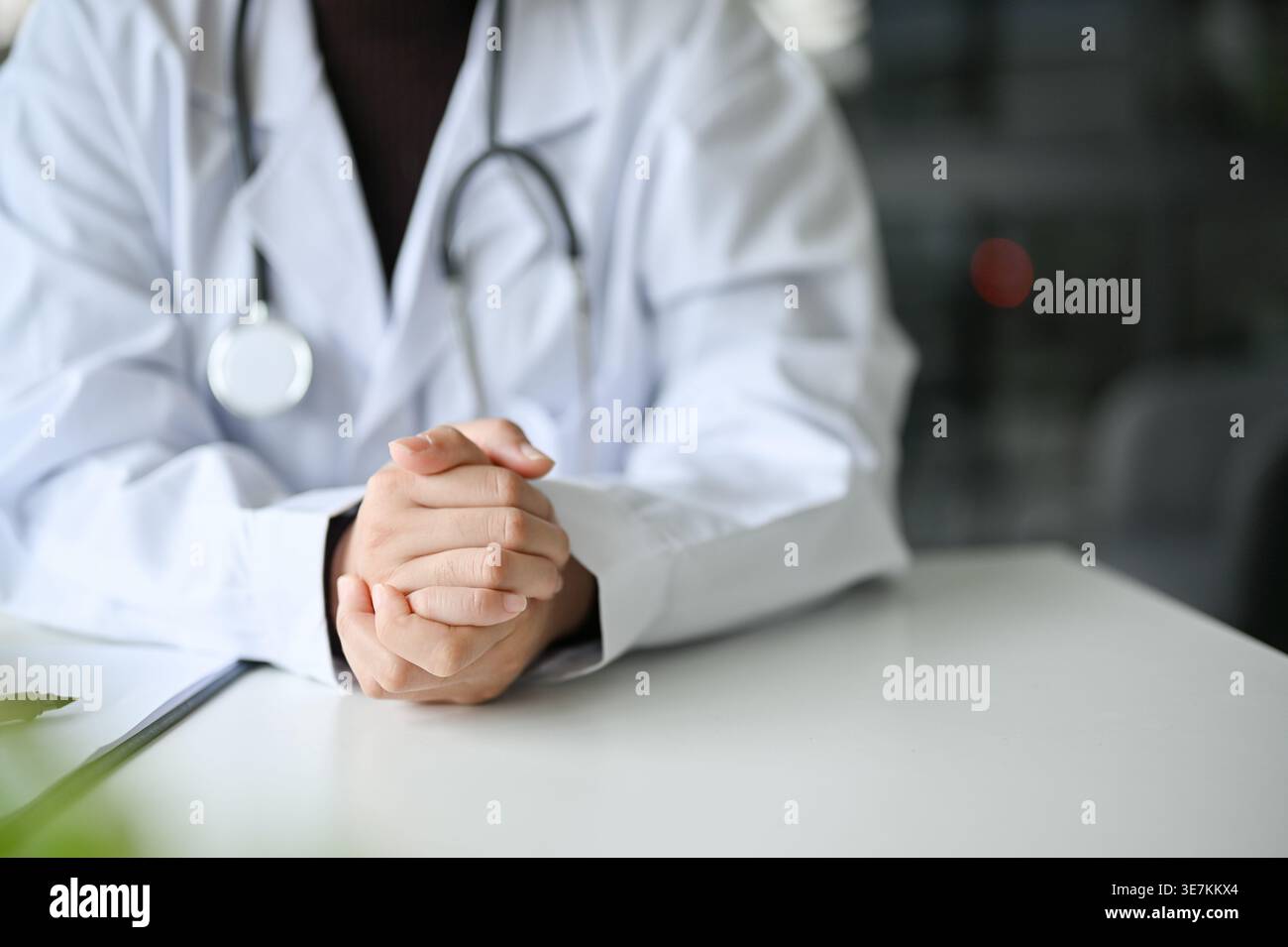Femme asiatique médecin assise avec les mains serrées à table en clinique Banque D'Images