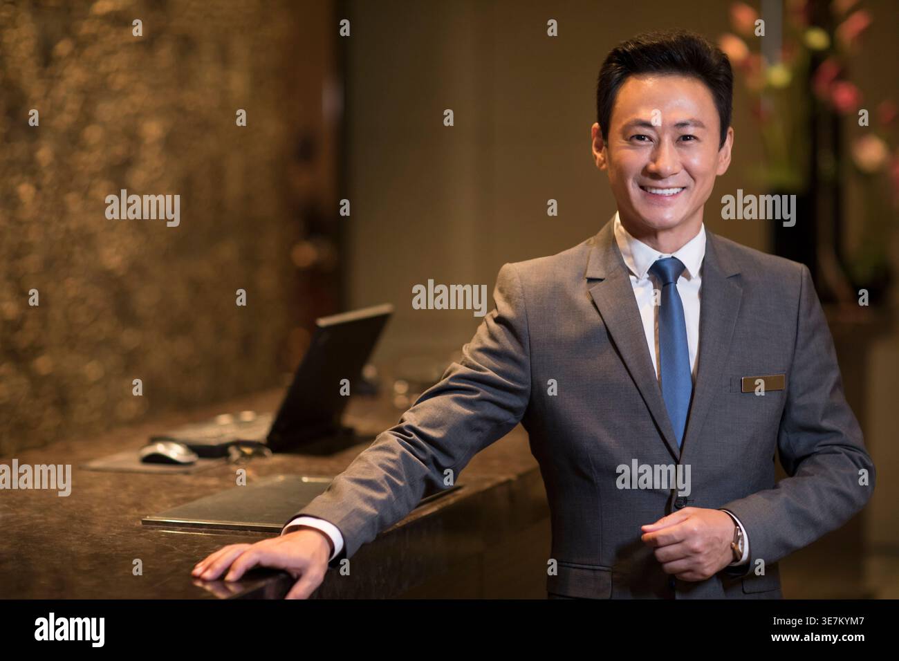 Le directeur d'hôtel chinois d'âge moyen souriant s'appuie sur la réception de l'hôtel Banque D'Images