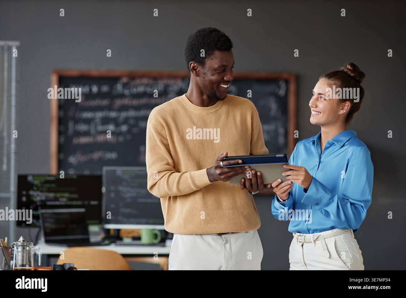 Programmeurs noirs masculins et féminins caucasiens utilisant la tablette se regardant les uns les autres tout en se tenant debout dans le bureau Banque D'Images