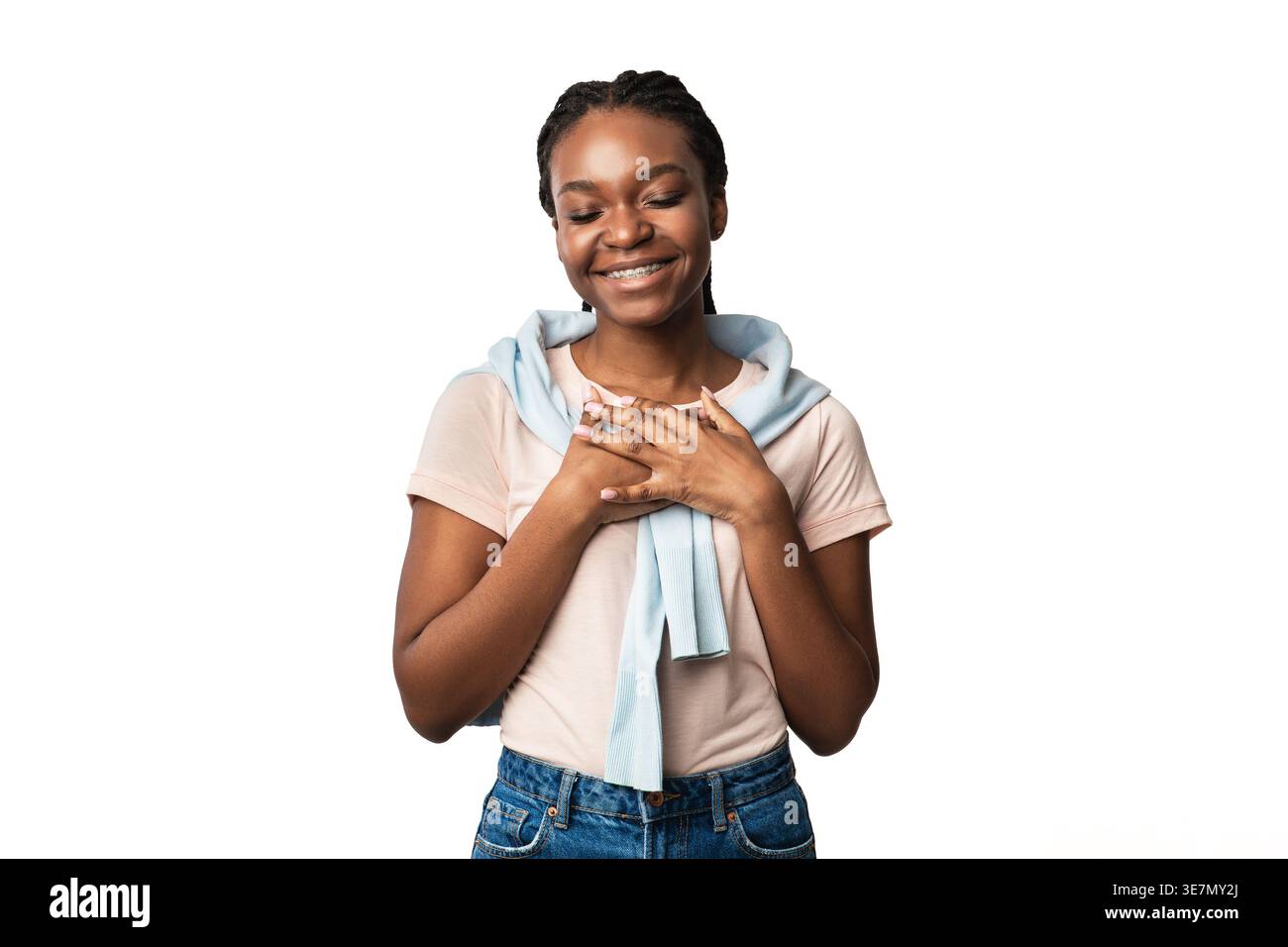 Femme noire souriante avec des appareils dentaires pressant les mains à la poitrine debout avec les yeux fermés sur fond blanc dans le studio Banque D'Images