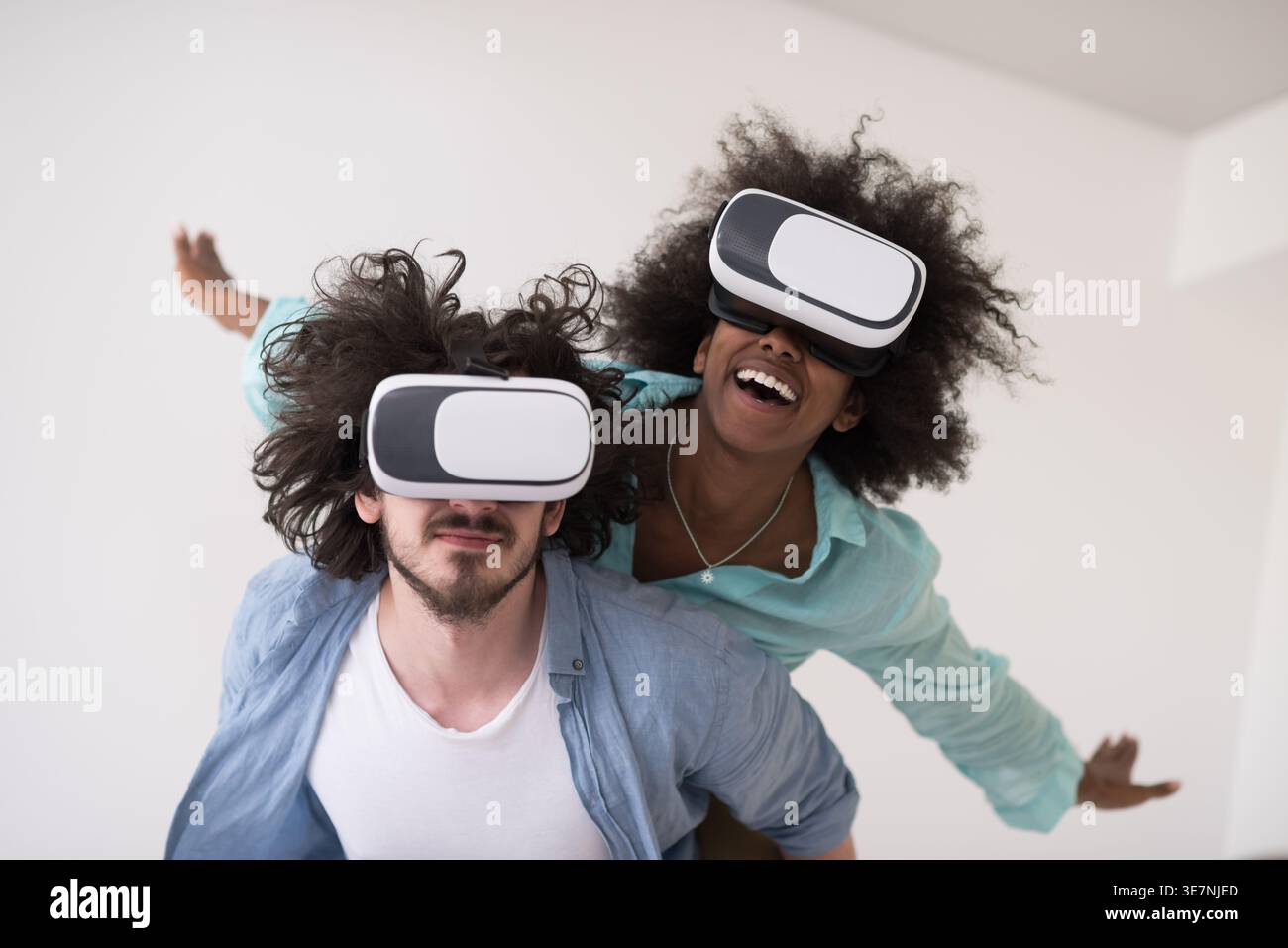 Couple noir et caucasien portant des casques VR ayant un plaisir piggyback équitation et expérimentant la réalité virtuelle sur fond blanc en studio Banque D'Images