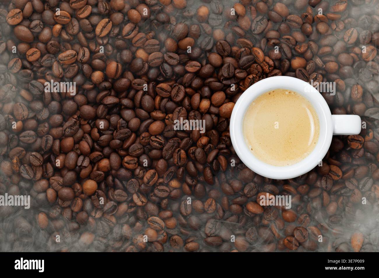 Espresso fraîchement préparé dans une tasse blanche, riche en crème se formant sur le dessus, entouré de grains de café torréfiés avec montée de vapeur. Vue de dessus Banque D'Images
