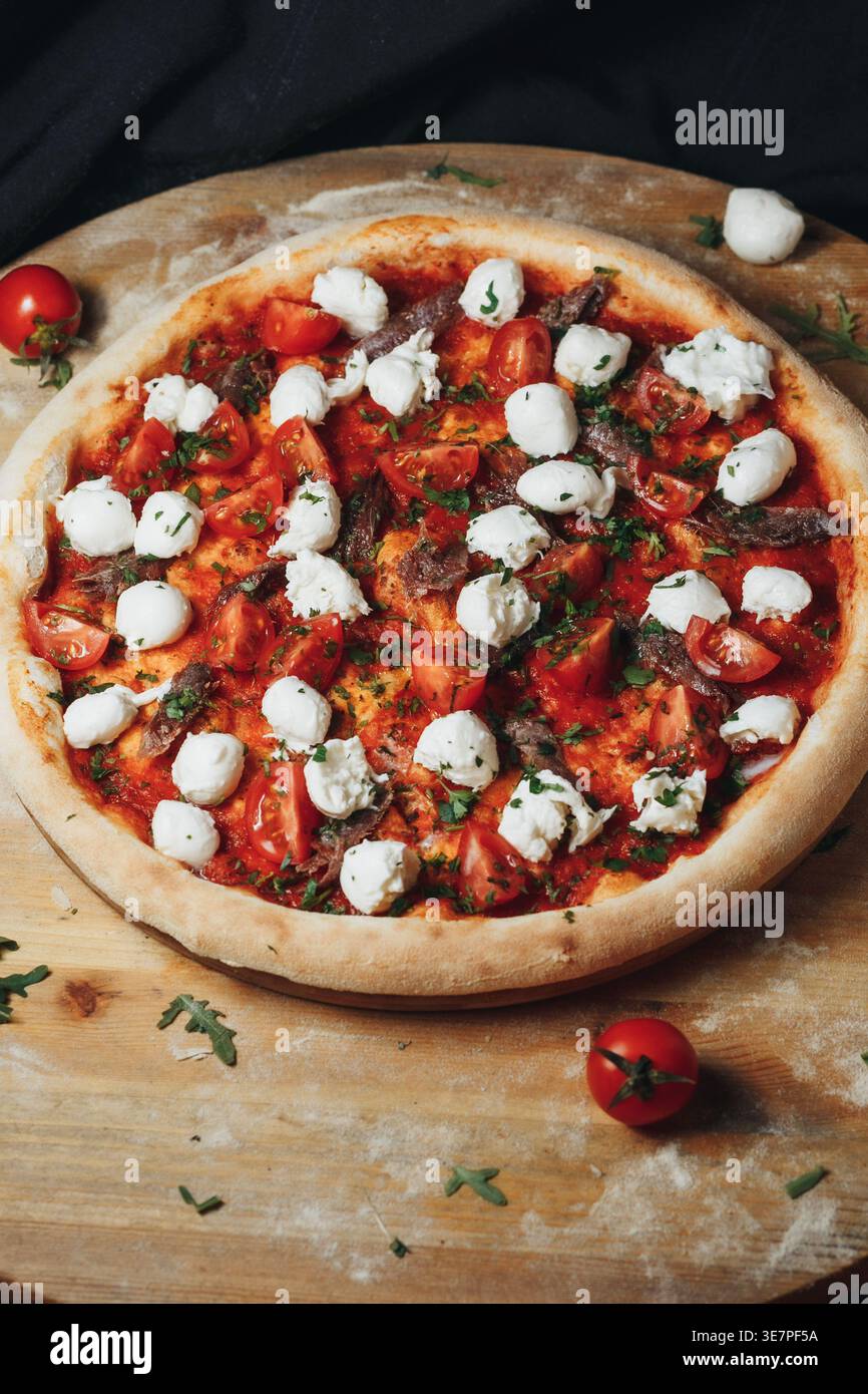 Pizza italienne fraîchement cuite avec une croûte dorée recouverte de sauce tomate riche boules de fromage mozzarella frais coupées en deux tomates cerises et anchois savoureux Banque D'Images