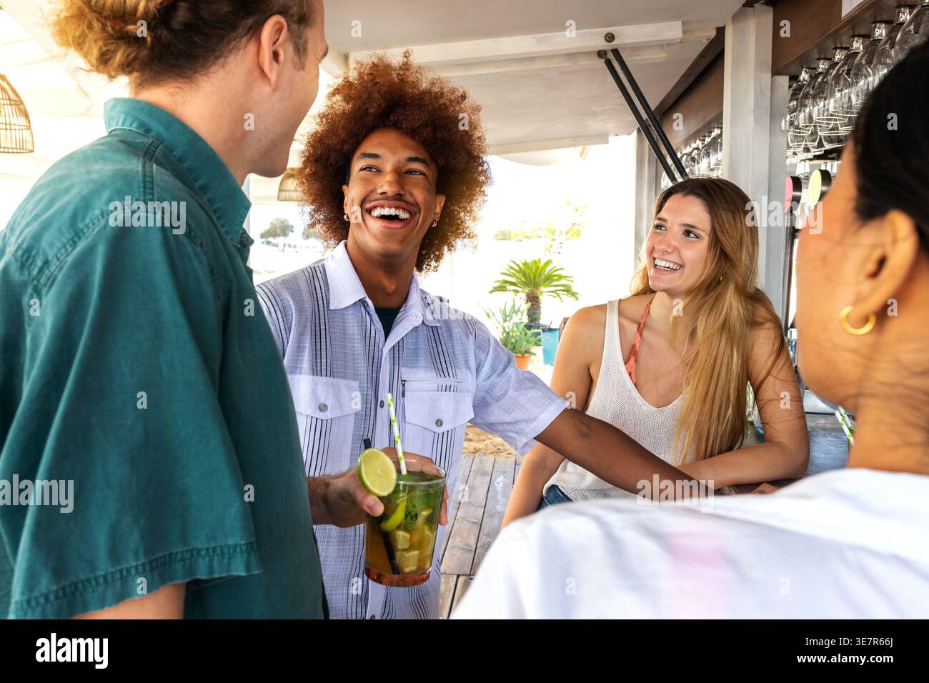 Groupe d'amis joyeux et divers discutant tout en se tenant près du comptoir et en prenant des cocktails mojito au bar de la plage pendant les vacances d'été Banque D'Images