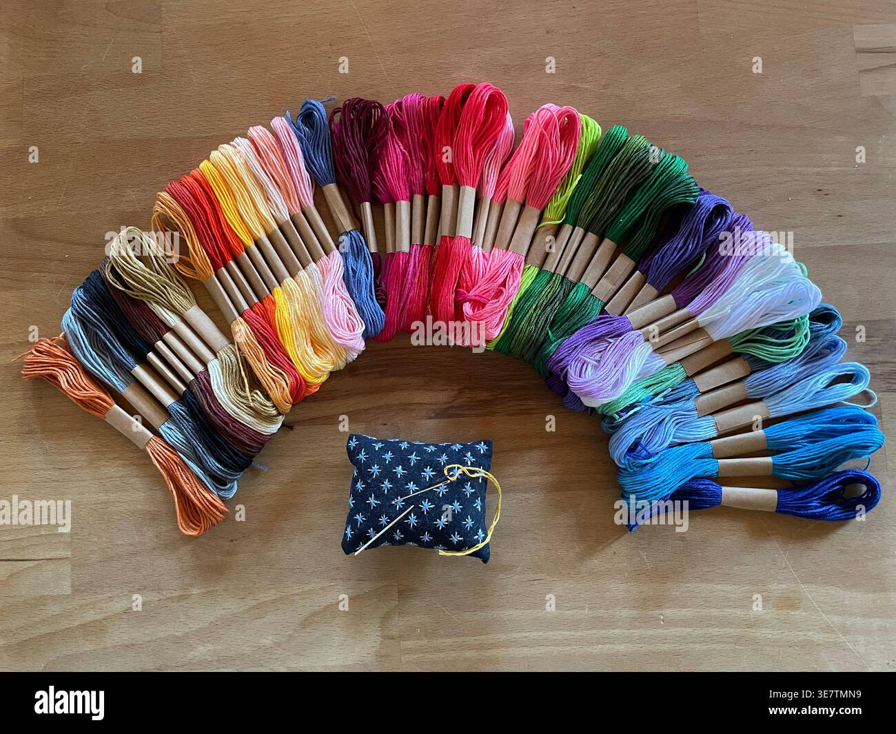 Arc-en-ciel vibrant d'écheveaux colorés de soie dentaire de broderie disposés en arc de cercle sur bois, avec un coussin d'épingle d'étoile. Banque D'Images