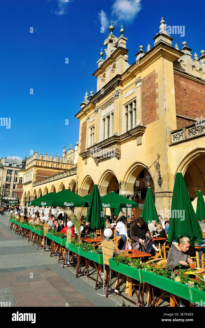 Les foules se rassemblent à des tables en plein air à Cracovie en Pologne. Les parapluies verts fournissent de l'ombre lorsque les gens mangent et parlent au soleil. Banque D'Images