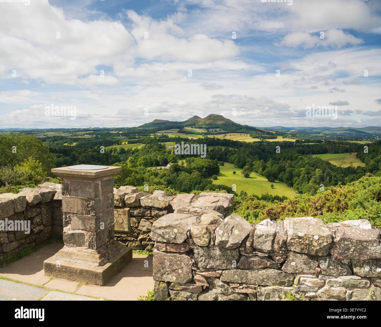 Un monument en pierre se dresse à un point de vue, offrant une vue panoramique sur des vallées verdoyantes, des forêts et des collines ondulantes sous un ciel nuageux Banque D'Images