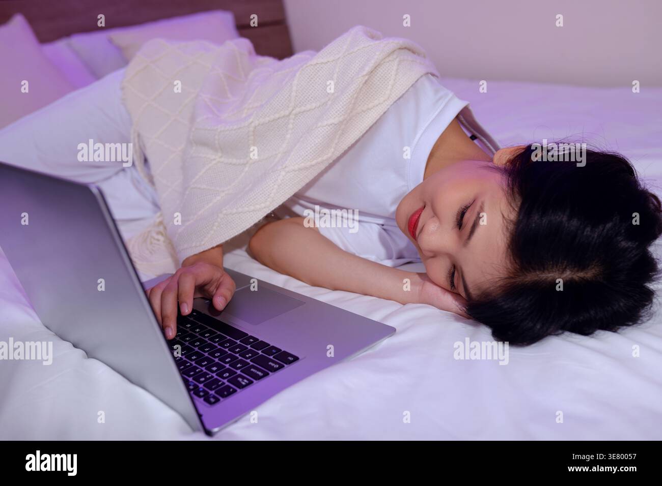 Femme asiatique souriante utilisant un ordinateur portable couché sur le lit à la maison Banque D'Images