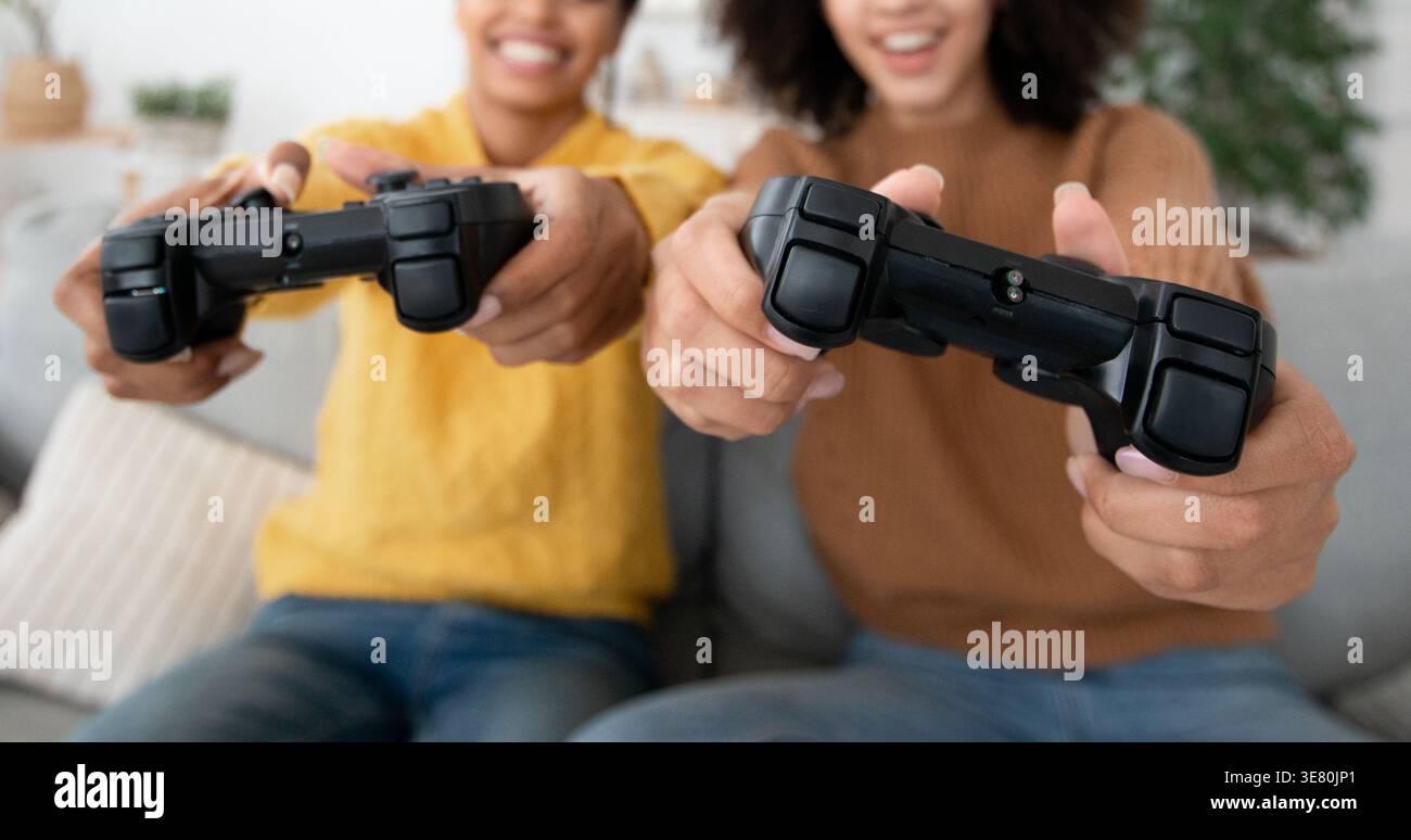 Amies noires utilisant la manette de jeu s'amusant tout en étant assis sur le canapé dans le salon à la maison Banque D'Images
