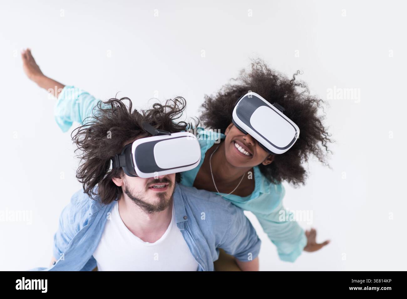 Couple noir et caucasien portant des casques VR ayant un plaisir piggyback équitation et expérimentant la réalité virtuelle sur fond blanc en studio Banque D'Images