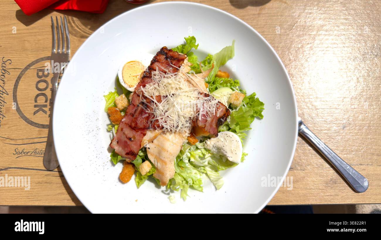 Vue aérienne d'une salade césar de poulet avec bacon grillé et fromage parmesan sur une assiette blanche à une table de marque Super Bock Banque D'Images