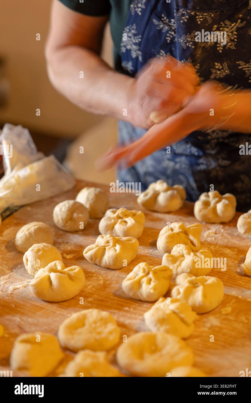 Mains de femme façonnant la pâte en kolaches sur une table en bois farinée Banque D'Images