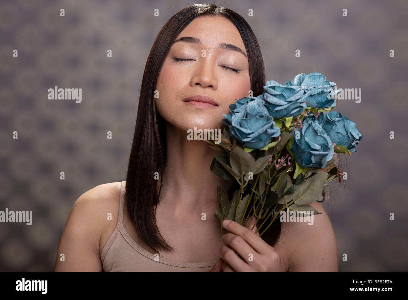 Modèle féminin joyeux avec la peau lisse et bouquet de fleurs décoratives de roses bleues, montrant la confiance en soi en studio. Le portrait responsabilisant célèbre la positivité corporelle et la beauté naturelle. Banque D'Images