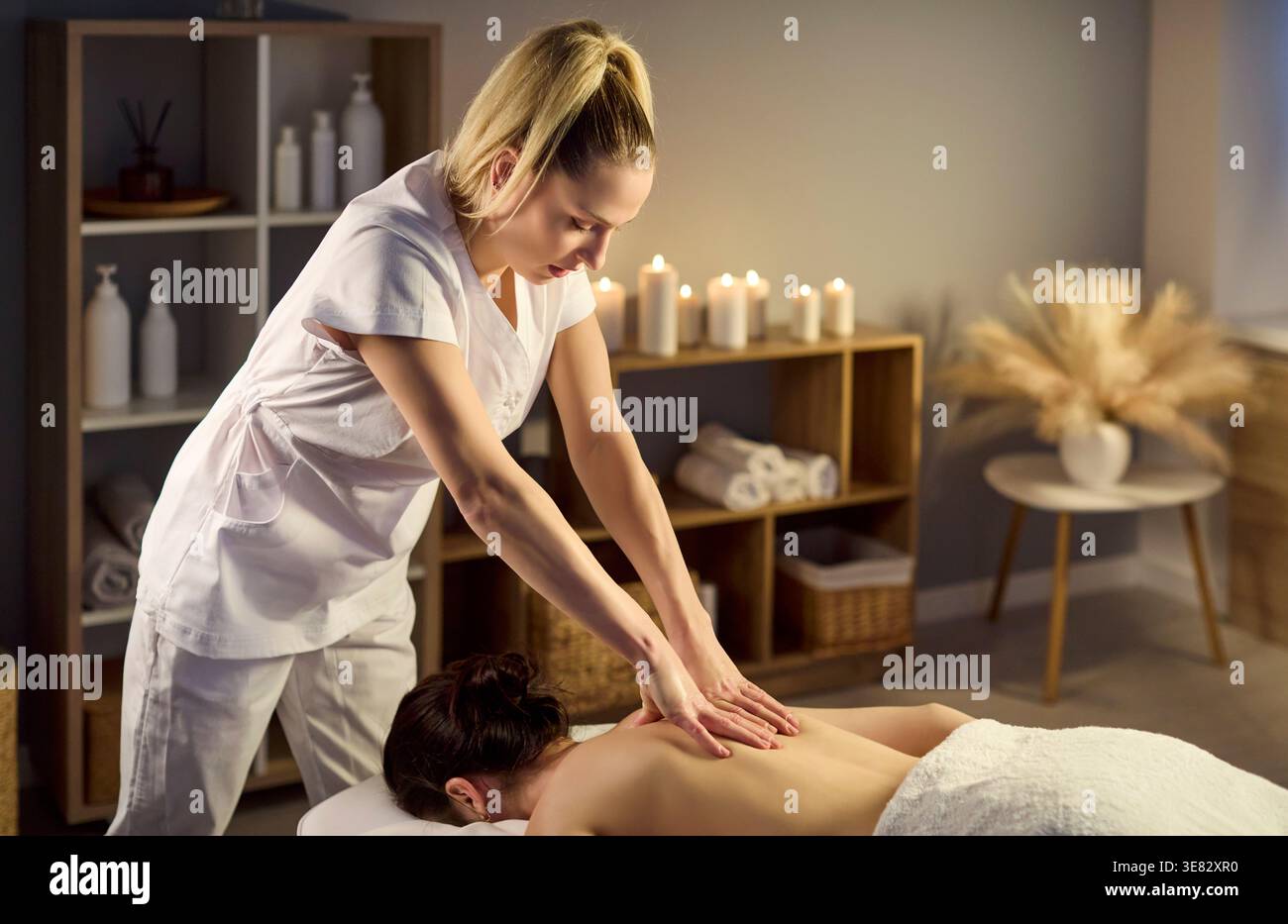 Masseuse professionnelle donnant massage relaxant du dos dans le spa avec bougies et décoration Banque D'Images