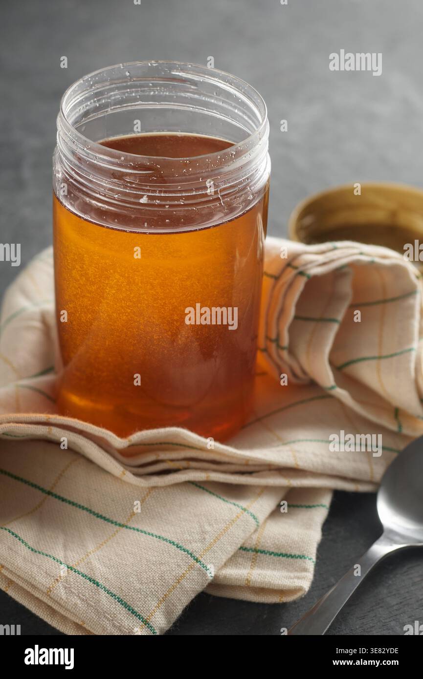 pot clair de miel avec serviette à carreaux sur la surface du dessus de table texturée sombre, édulcorant liquide dans un récipient en verre, soft focus avec espace de copie, sain Banque D'Images
