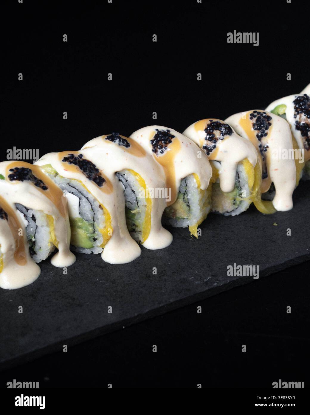 Rouleaux de sushi avec sauce crémeuse et caviar noir. L'ardoise noire offre un contraste élégant. Chaque pièce est agencée avec art, invitant les spectateurs. Parfait pour Banque D'Images