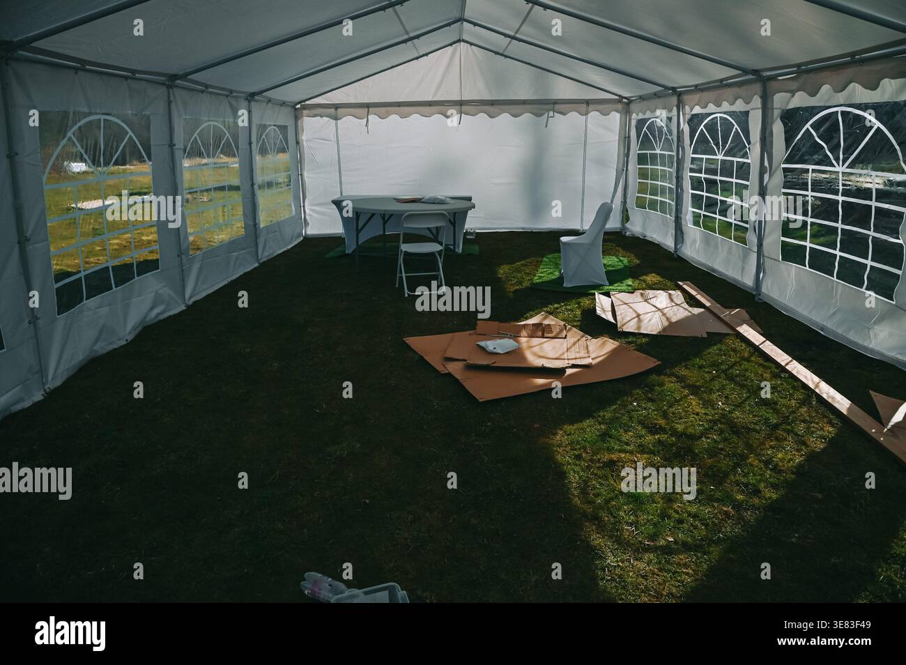 Intérieur de tente blanche spacieuse d'événement avec tables pliantes, chaises et matériaux de configuration sur l'herbe. Parfait pour les thèmes de préparation d'événement, functio extérieur Banque D'Images