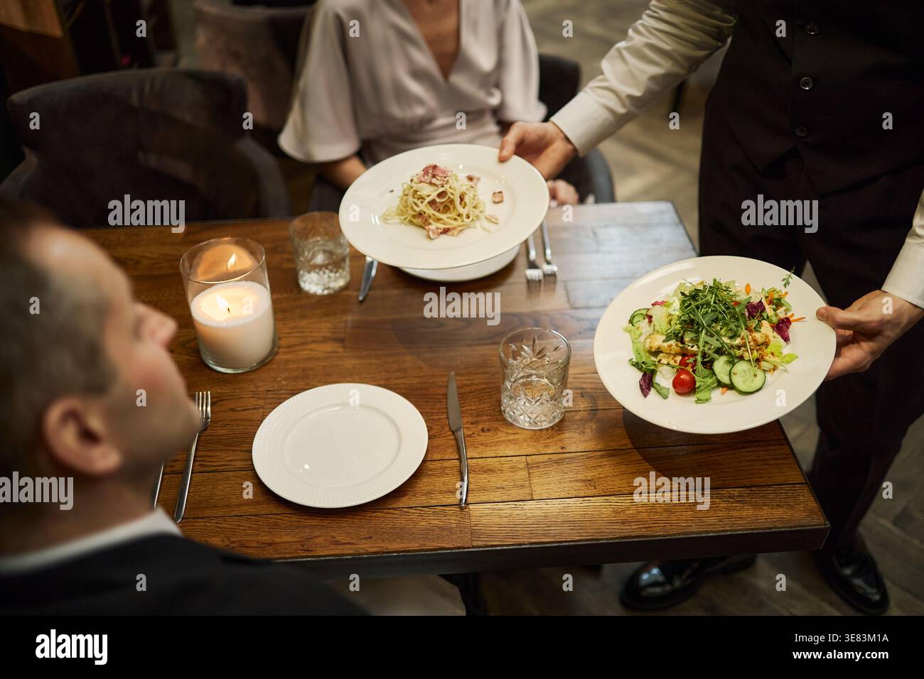Serveur servant le dîner à un couple adulte au restaurant pour la soirée Banque D'Images