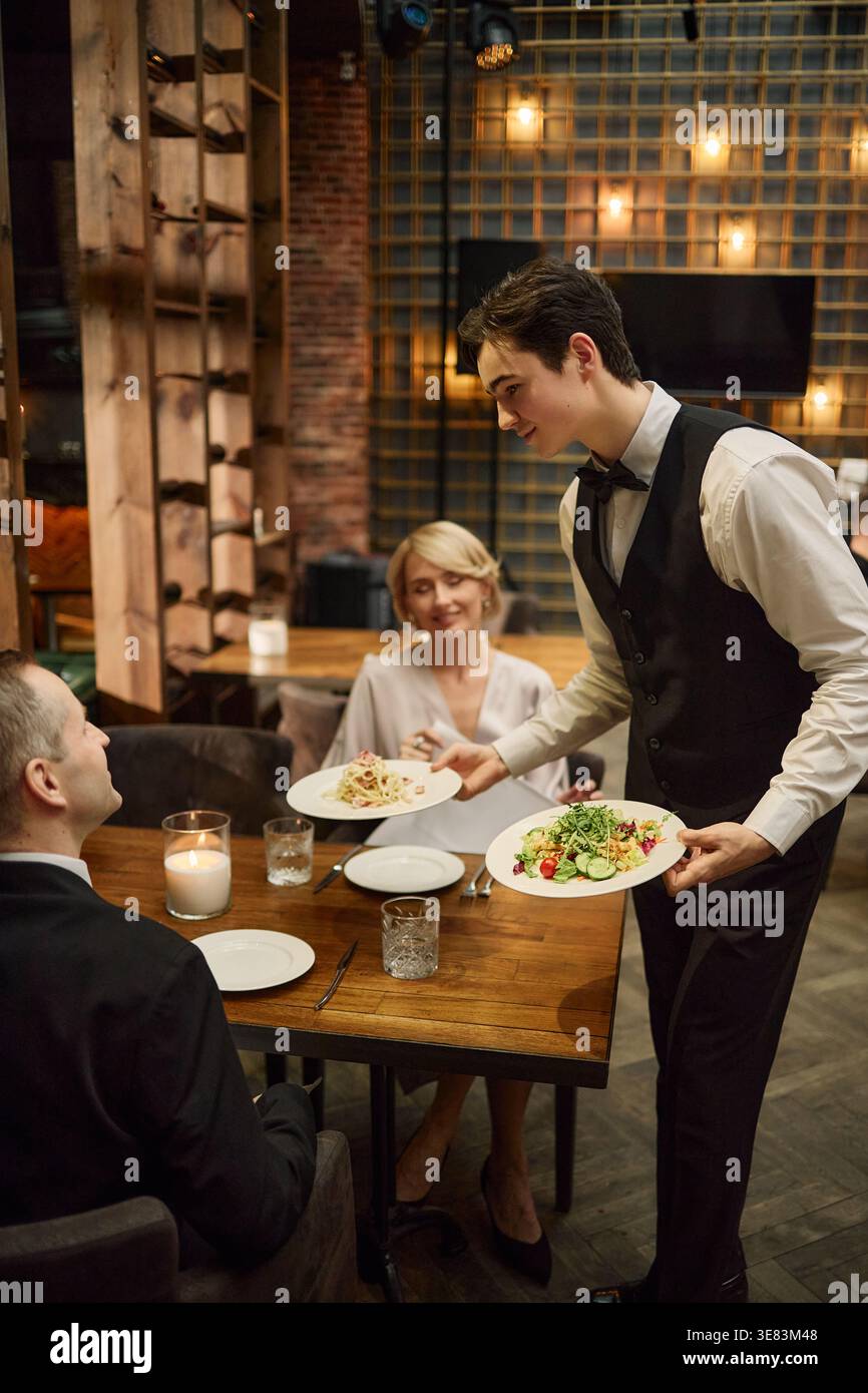 Serveur adulte servant le dîner pour couple au restaurant Hospitality Banque D'Images