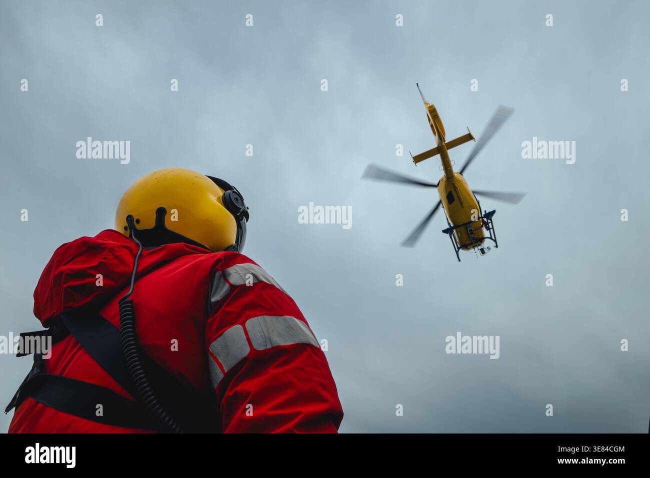 Vue arrière du paramédical en uniforme rouge et casque regardant l'hélicoptère d'ambulance aérienne décoller. Thèmes sauvetage, aide et espoir. Banque D'Images