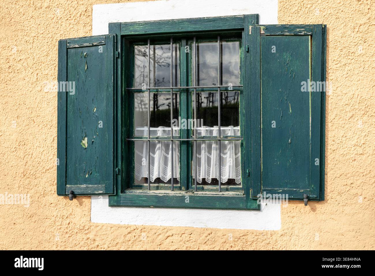 Un volet en bois vieilli et peint sarcelle est ouvert, révélant une fenêtre avec des barres de fer et de délicats rideaux blancs. La fenêtre est placée dans un texturé, PA Banque D'Images