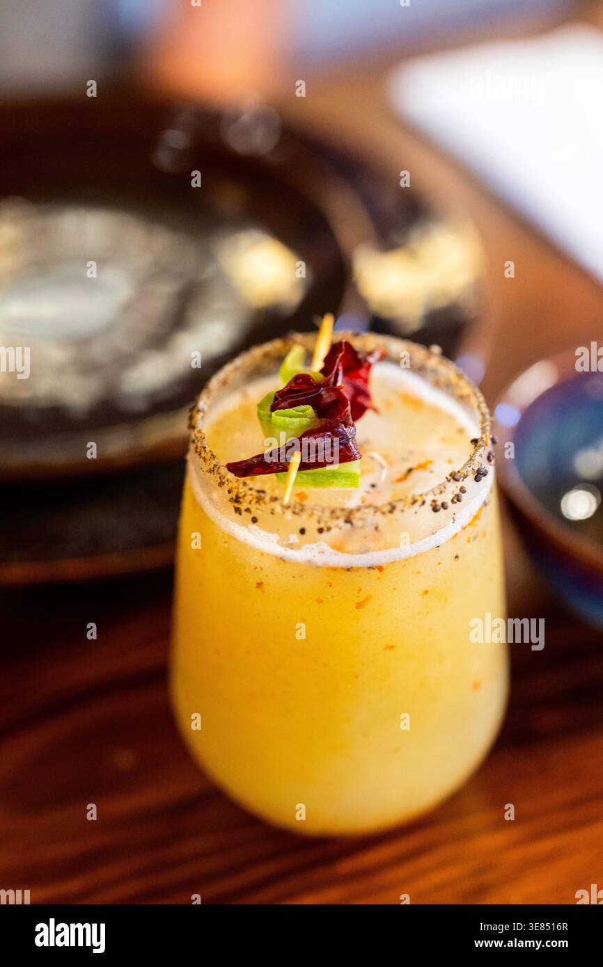 Gros plan d'un cocktail tropical jaune dans un verre court avec un bord épice-sel et garniture de fleur comestible sur une table en bois, faible profondeur de champ dans un Banque D'Images