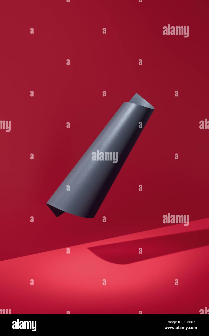 Scène 3D minimaliste avec un ruban de papier noir incurvé flottant sur un fond rouge riche, projetant une ombre douce. Formes abstraites modernes pour affiche, son Banque D'Images