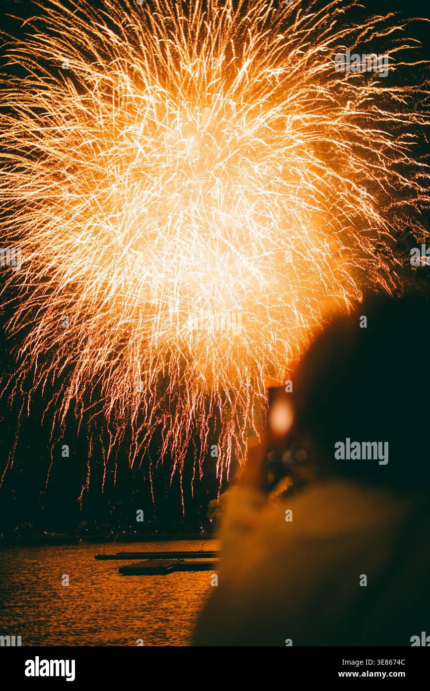 De brillants feux d'artifice dorés explosent à travers un ciel nocturne sombre au-dessus de l'eau calme, créant une scène de célébration rayonnante avec des sentiers étincelants et une lueur chaude Banque D'Images