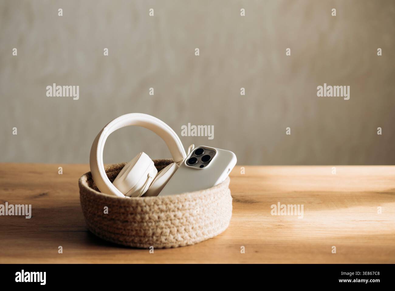 Un smartphone et un casque reposent dans un panier tissé sur une table en bois, symbolisant une détox numérique à la maison. Ce réglage calme met en évidence l'équilibre BE Banque D'Images