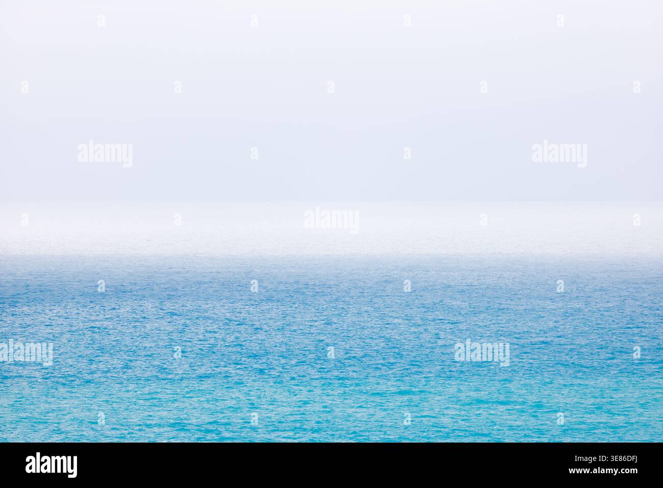 Cette photo minimaliste montre la mer Méditerranée bleue au large de la côte de Villajoyosa sous un ciel lumineux et brumeux. La texture de l'eau est proéminente, et le Banque D'Images