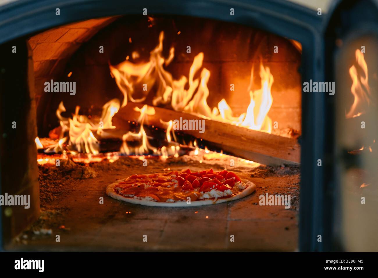 Pizza fraîche au four à bois traditionnel avec des flammes vives et des braises incandescentes. Banque D'Images