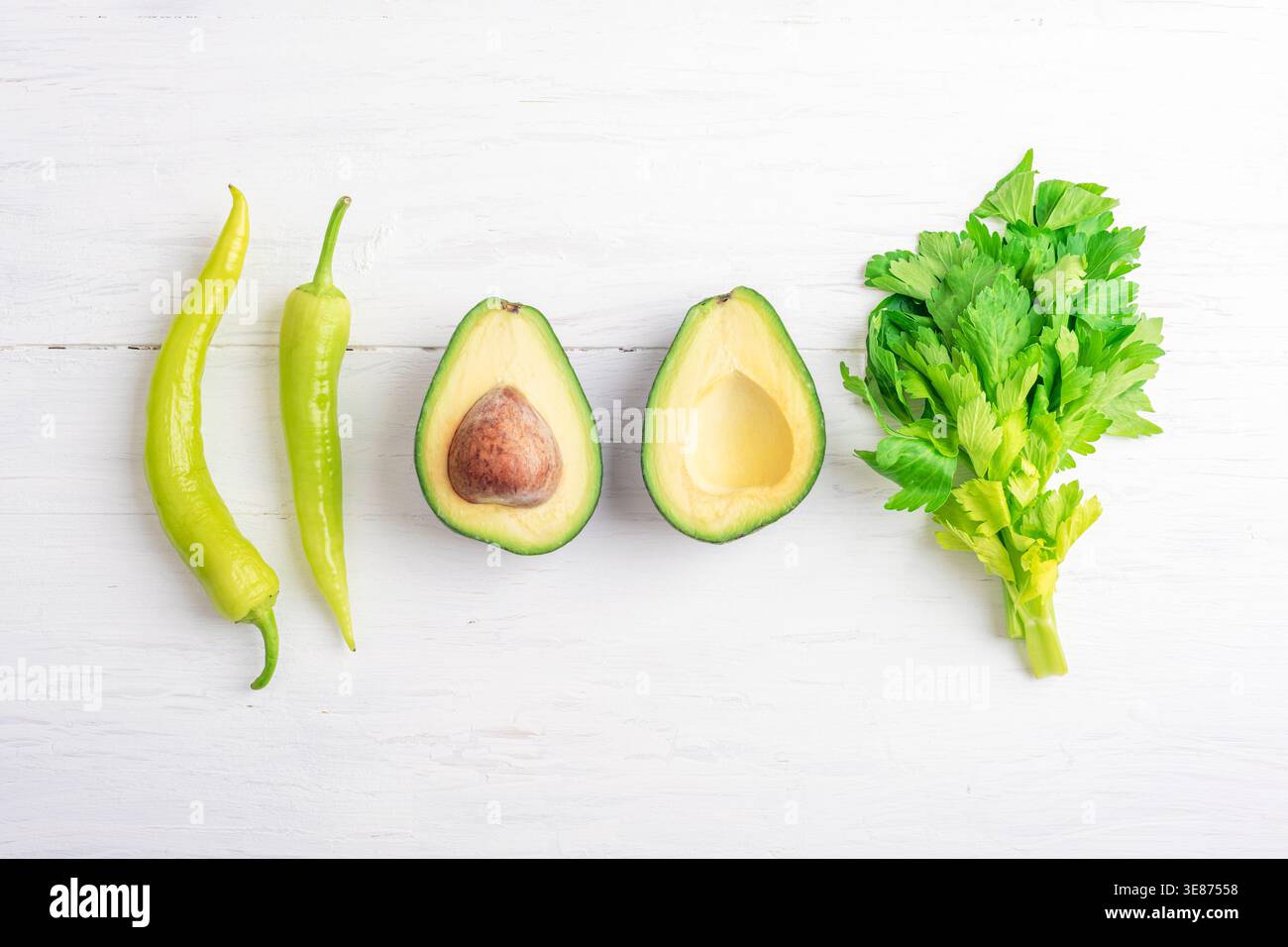 Piment fort, avocat et légumes verts de céleri sur table en bois blanc. Concept de nourriture végétarienne saine. Vue de dessus, pose à plat. Banque D'Images