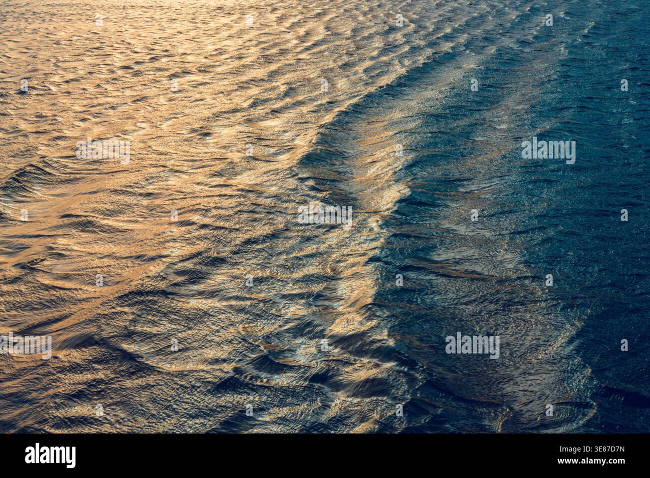 Gros plan des vagues de l'océan douces avec la lumière dorée du soleil reflétant sur la surface ondulée de l'eau. Banque D'Images