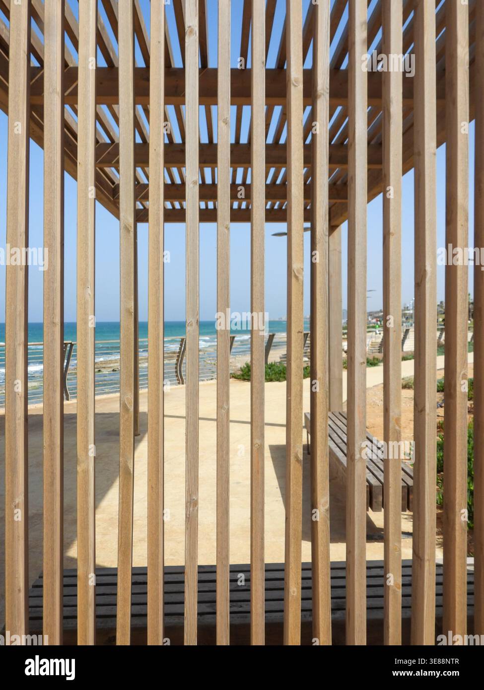 Les lattes de pergola en bois forment un cadre géométrique linéaire au-dessus d'une promenade côtière avec des bancs, menant l'œil à la mer Méditerranée bleue et au Hori clair Banque D'Images