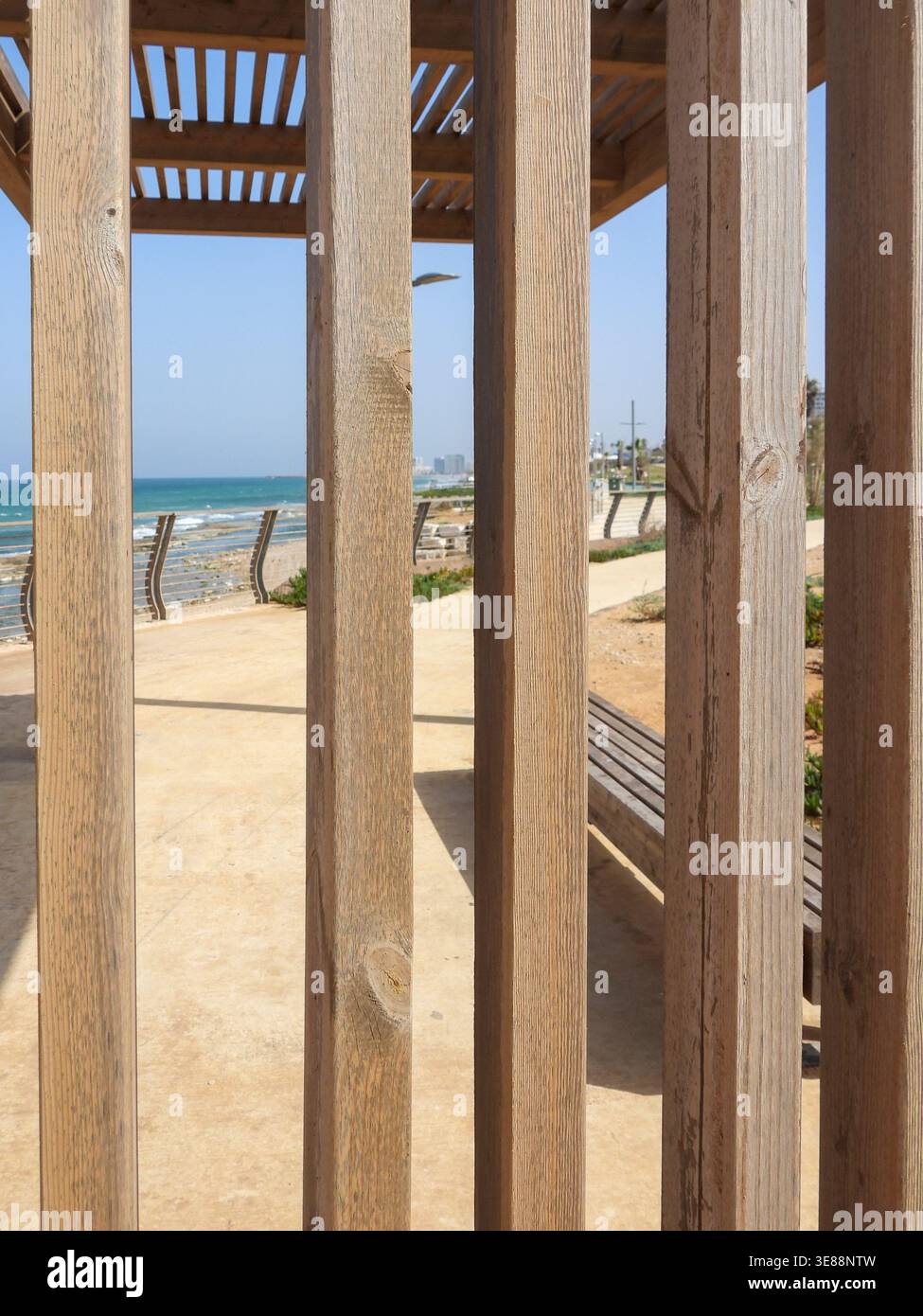 Les lattes de pergola en bois forment un cadre géométrique linéaire au-dessus d'une promenade côtière avec des bancs, menant l'œil à la mer Méditerranée bleue et au Hori clair Banque D'Images