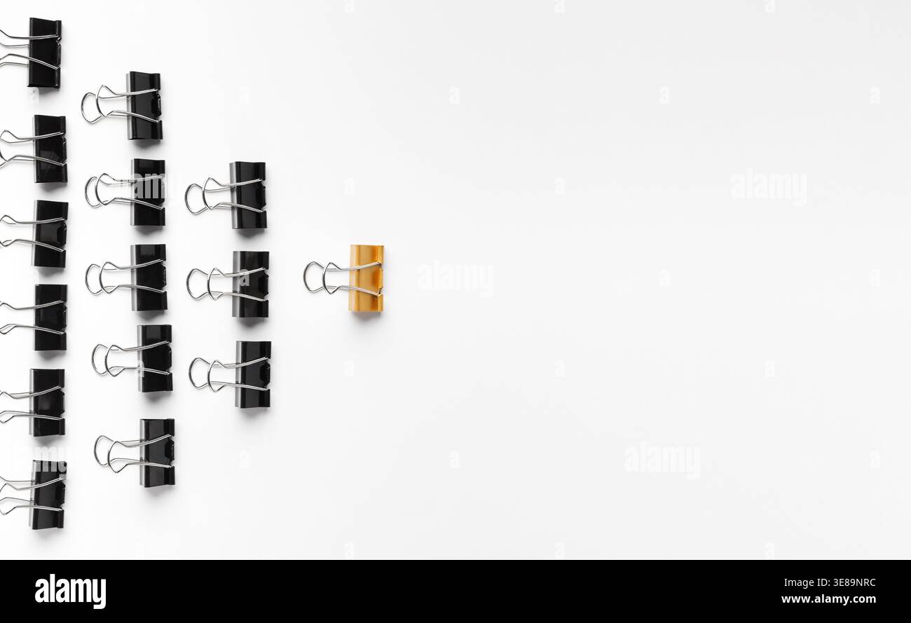 Collage de clips de reliure disposés sur une surface blanche mettant en évidence un clip orange unique Banque D'Images
