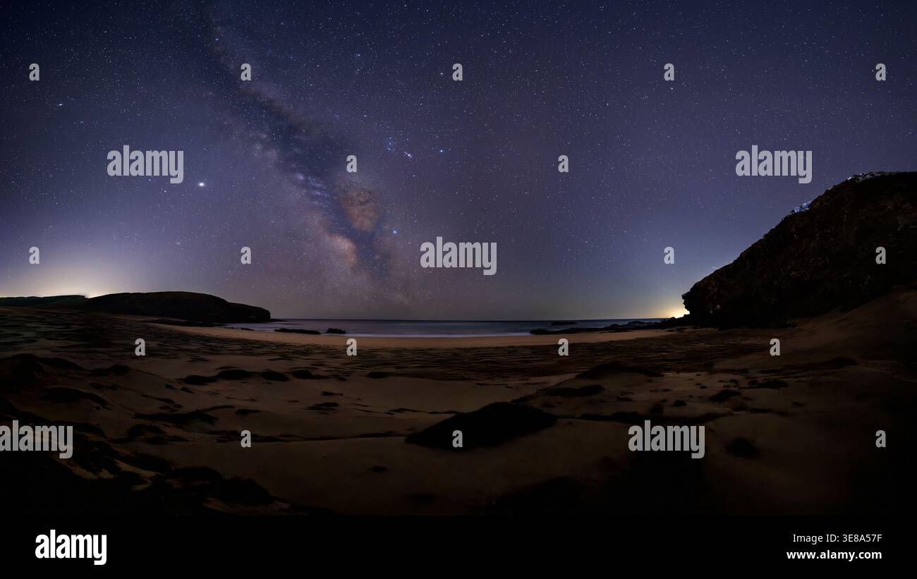 La voie lactée est visible à travers un ciel nocturne rempli d'étoiles au-dessus d'une plage de sable et d'une mer calme. La longue exposition capture un paysage côtier tranquille avec Banque D'Images