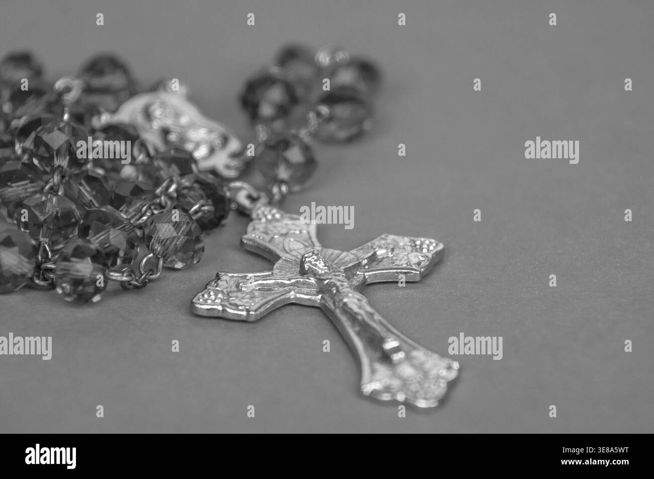 Chapelet monochrome avec crucifix métallique et perles réfléchissantes affichées sur fond neutre dans une nature morte religieuse noire et blanche dramatique. Banque D'Images