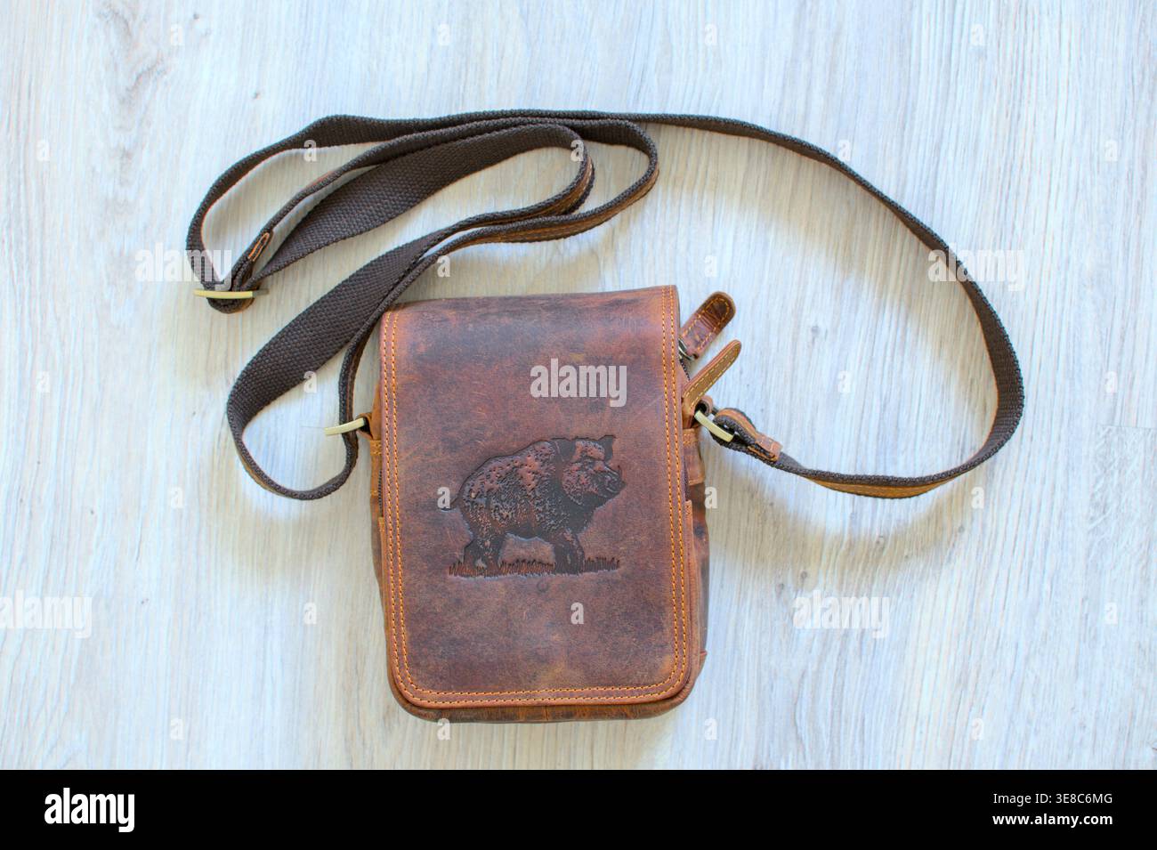 Vue aérienne du sac messager en cuir brun rustique pour hommes sur un sol en bois gris. Accessoire de voyage et d'extérieur de style vintage. Banque D'Images